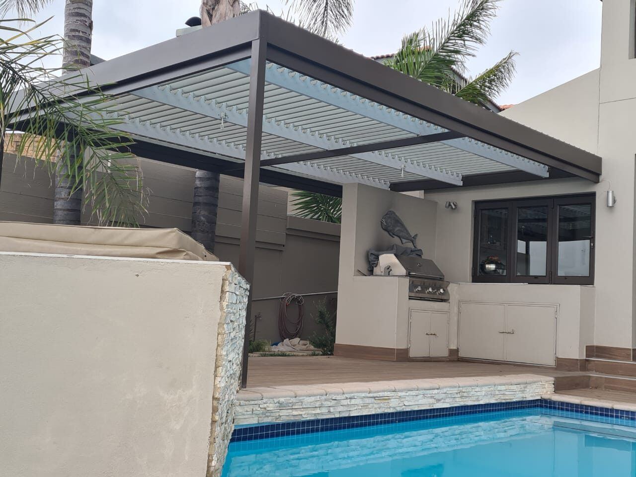 Bronze frame, white blades aluminium louvre roof over a patio in Melkbosstrand, Cape Town.