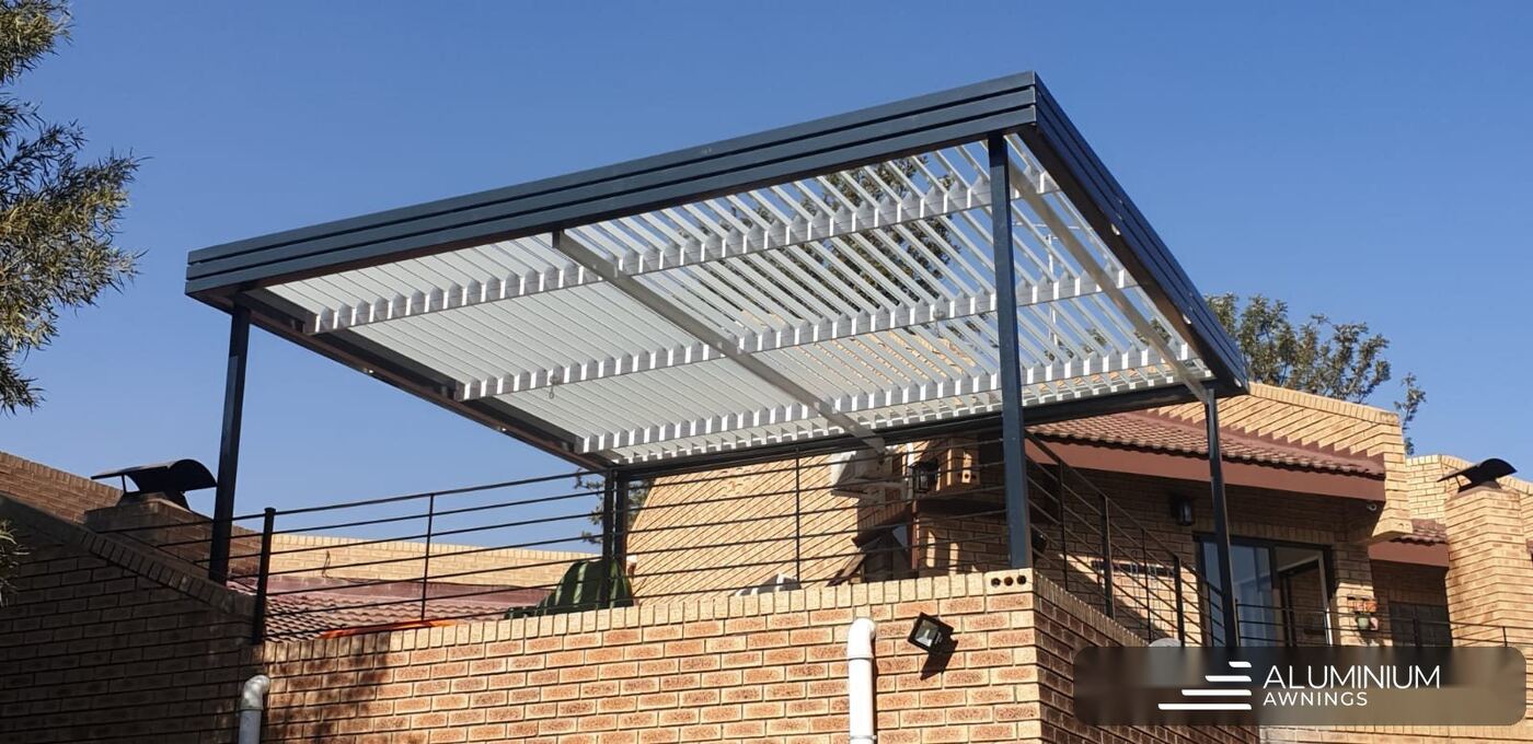 Freestanding aluminium louvre roof in Bellville with a charcoal frame and white blades over a paved area.